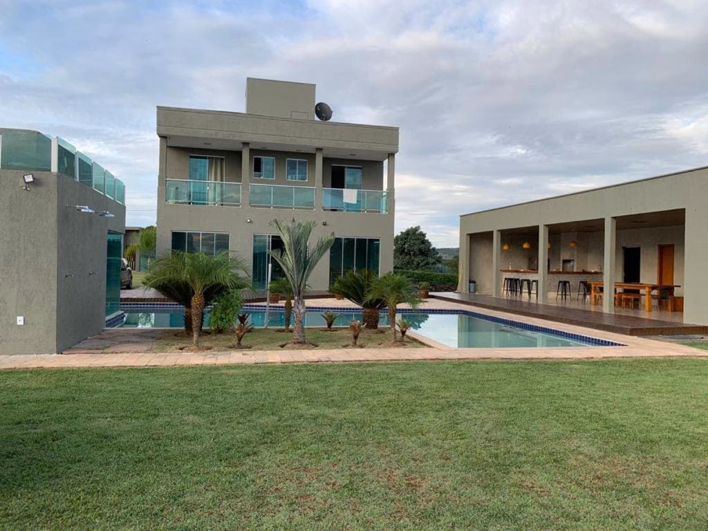 Vista externa da casa com piscina, palmeiras e jardim gramado