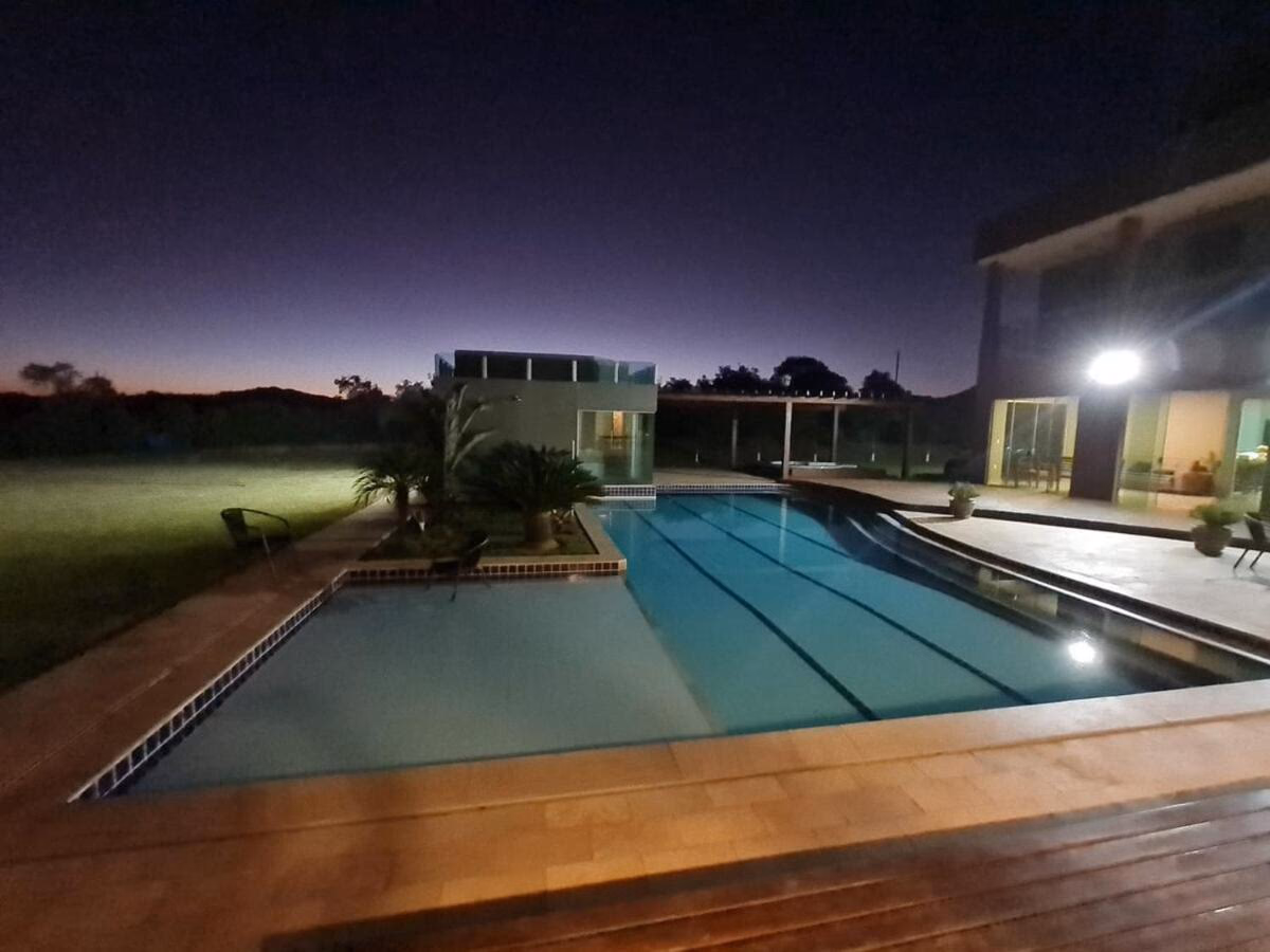 Piscina iluminada ao entardecer, com a casa ao fundo