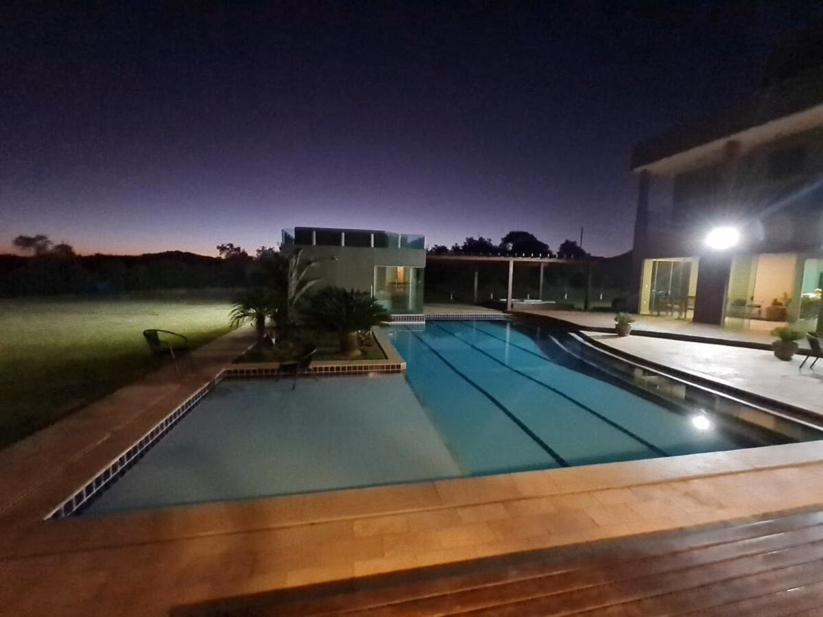 Piscina iluminada ao entardecer, com a casa ao fundo