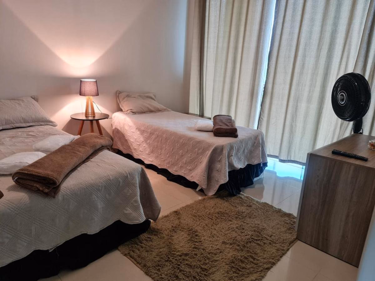 Quarto com camas de casal, abajur aceso e ventilador