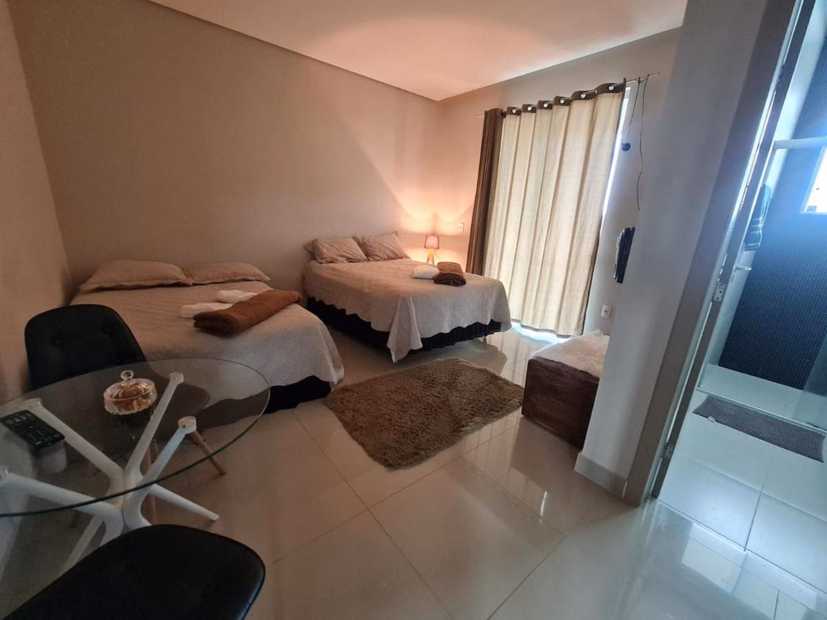 Quarto com cama de casal e cama de solteiro, luminária de mesa acesa